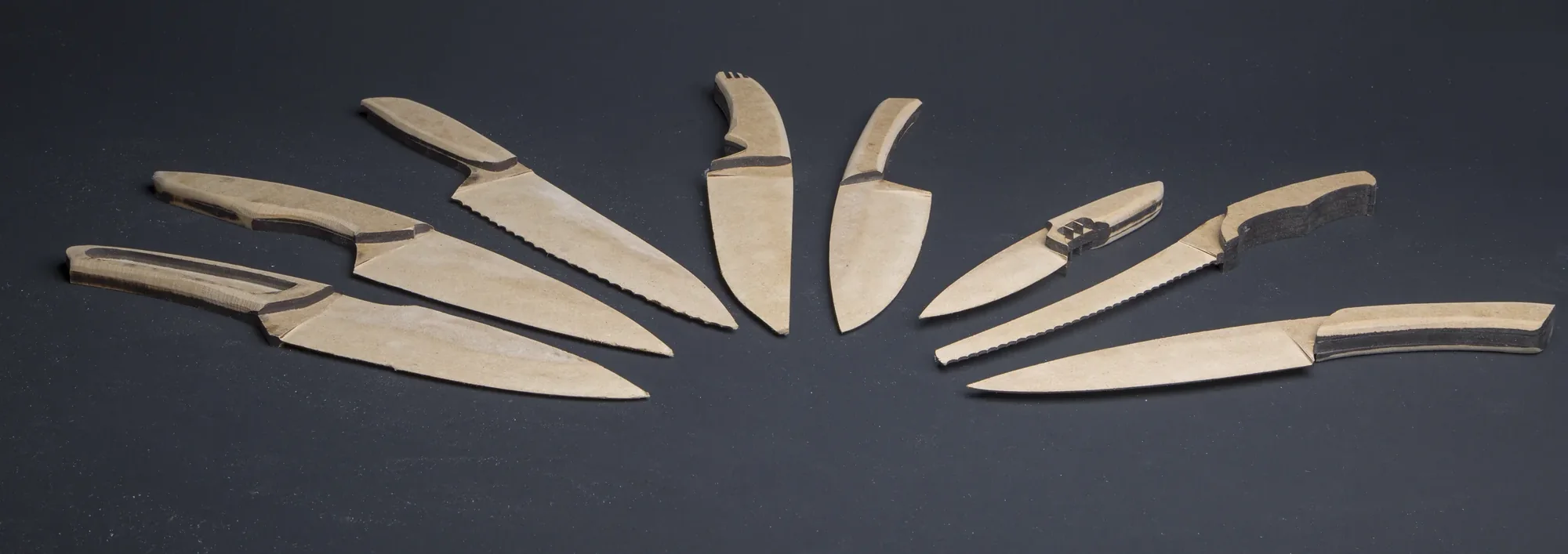 Fan of carved wooden knife prototypes spread on grey