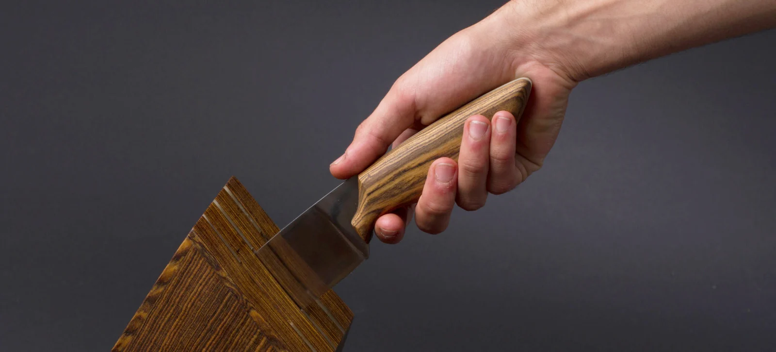 A hand holding the finished knife in a pinch grip