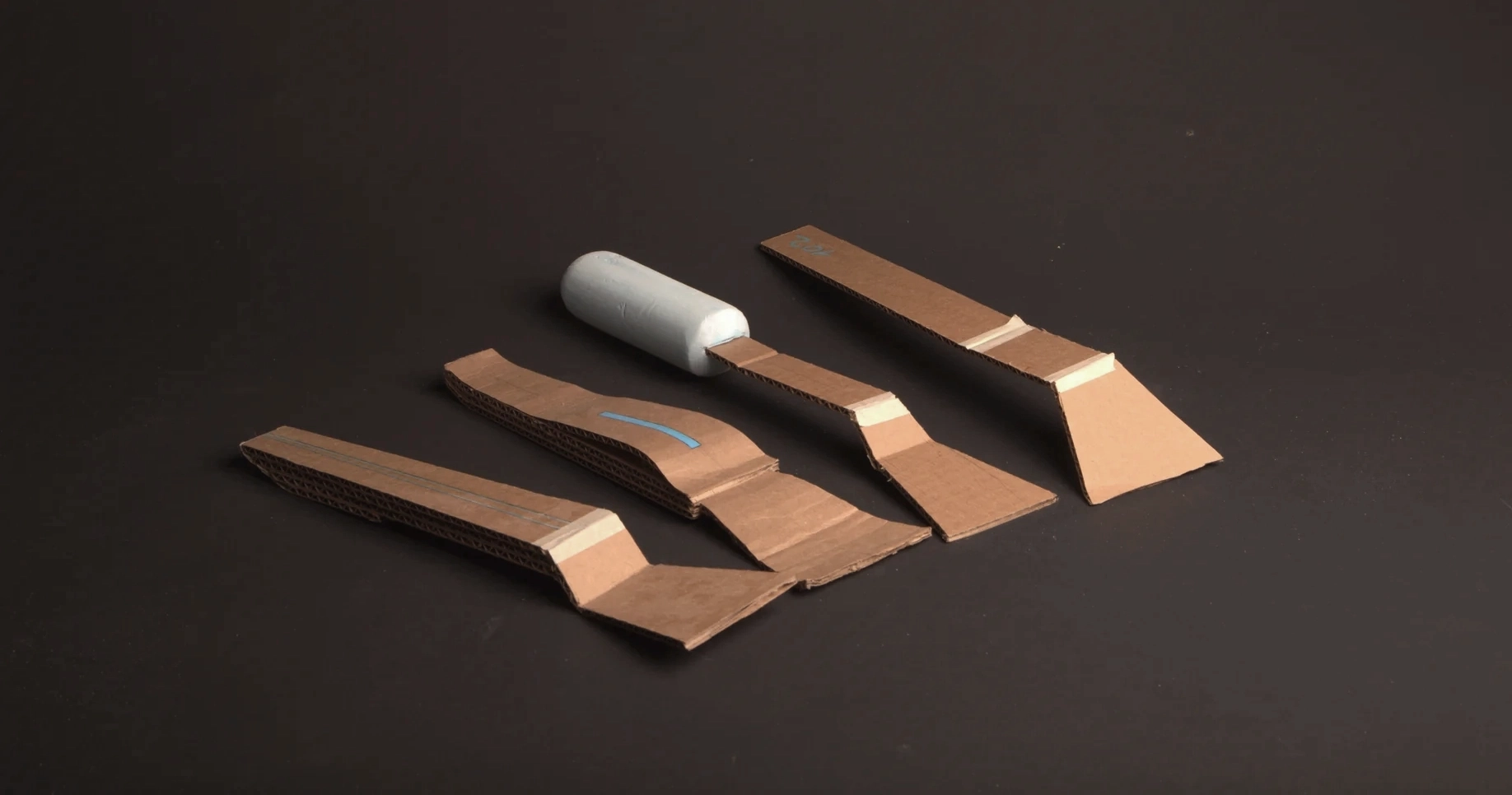 Four cardboard handle mockups laid out on grey, one with a clay grip